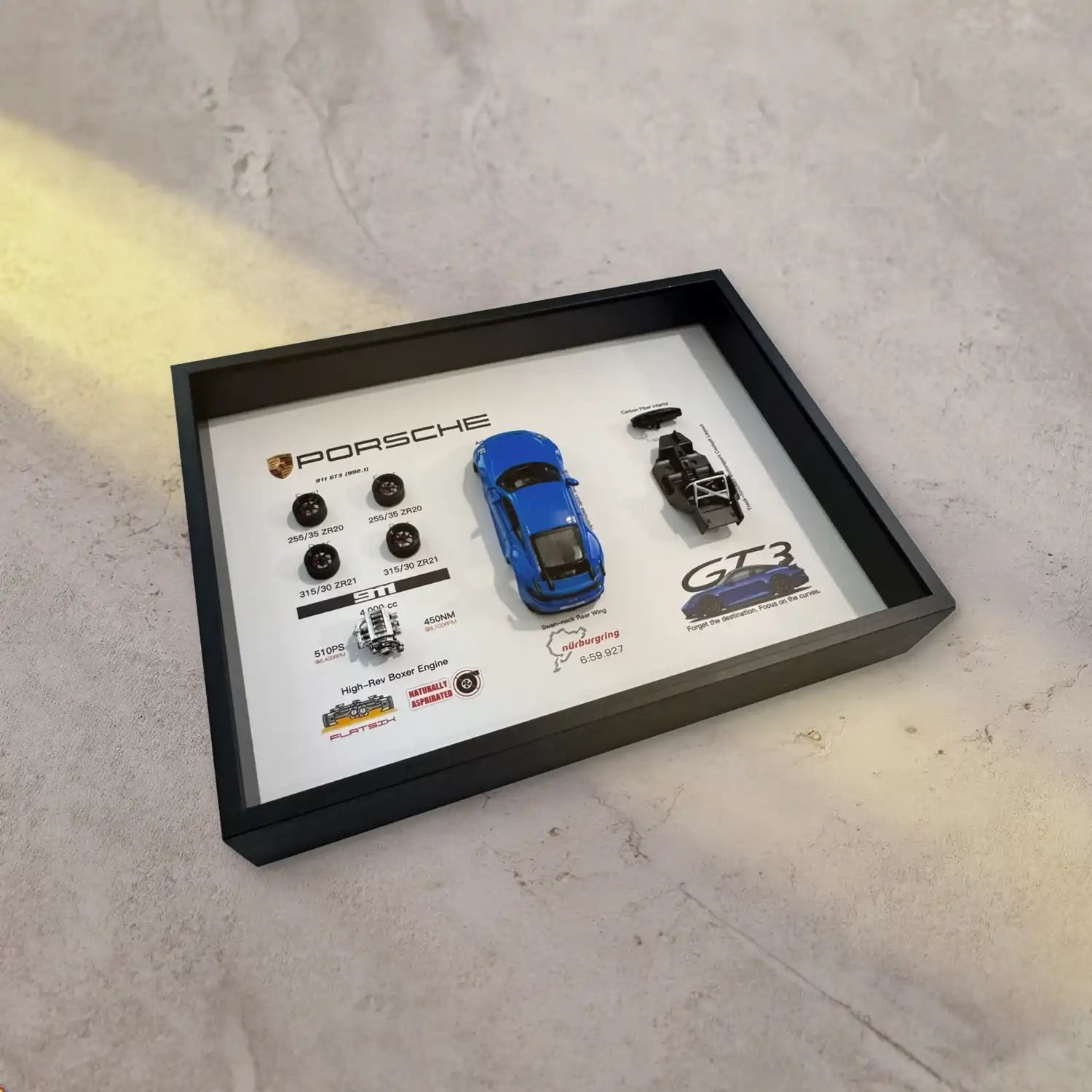 Porsche 911 GT3 992 Shark Blue Deconstructed Frame — laid on grey concrete under a warm light beam, frame depth visible