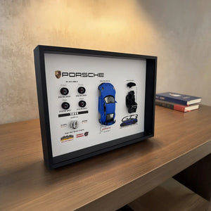 Porsche 911 GT3 992 Shark Blue Deconstructed Frame — standing on a walnut shelf with books to the right under warm wall light